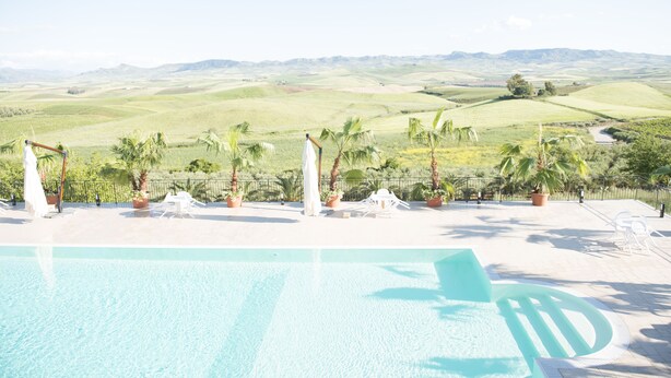 Un espace piscine offrant une vue sur des collines verdoyantes et des palmiers.