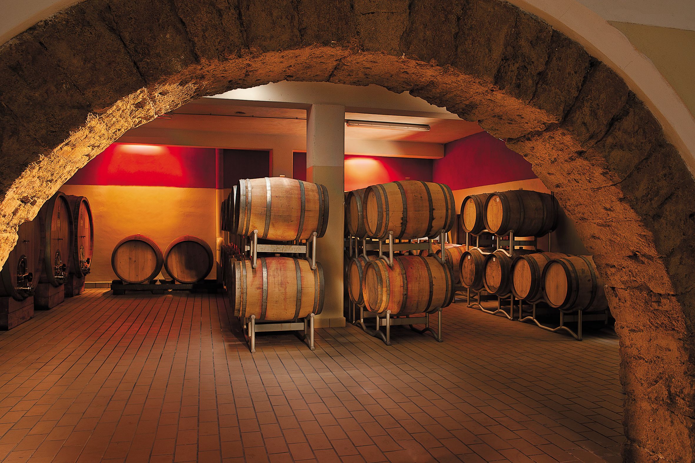 Una cantina vinicola con botti di legno e pavimento in mattoni.