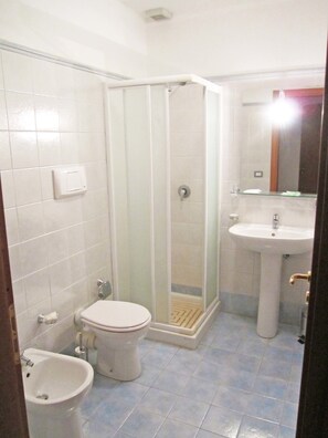 Een badkamer met toilet, bidet, wastafel en een douchecabine met glazen wanden.