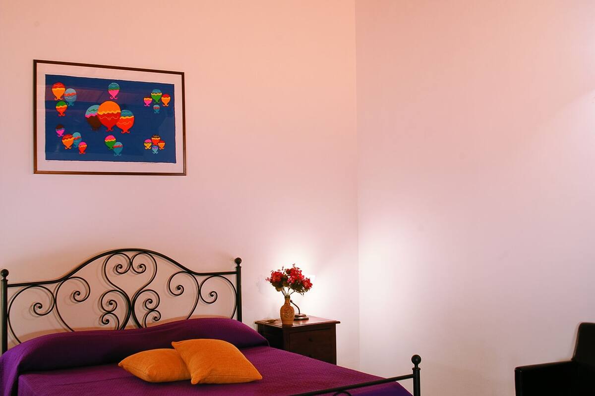 Ein Schlafzimmer mit Bett, Nachttisch, Sessel, Holzboden und einem Wandbild.