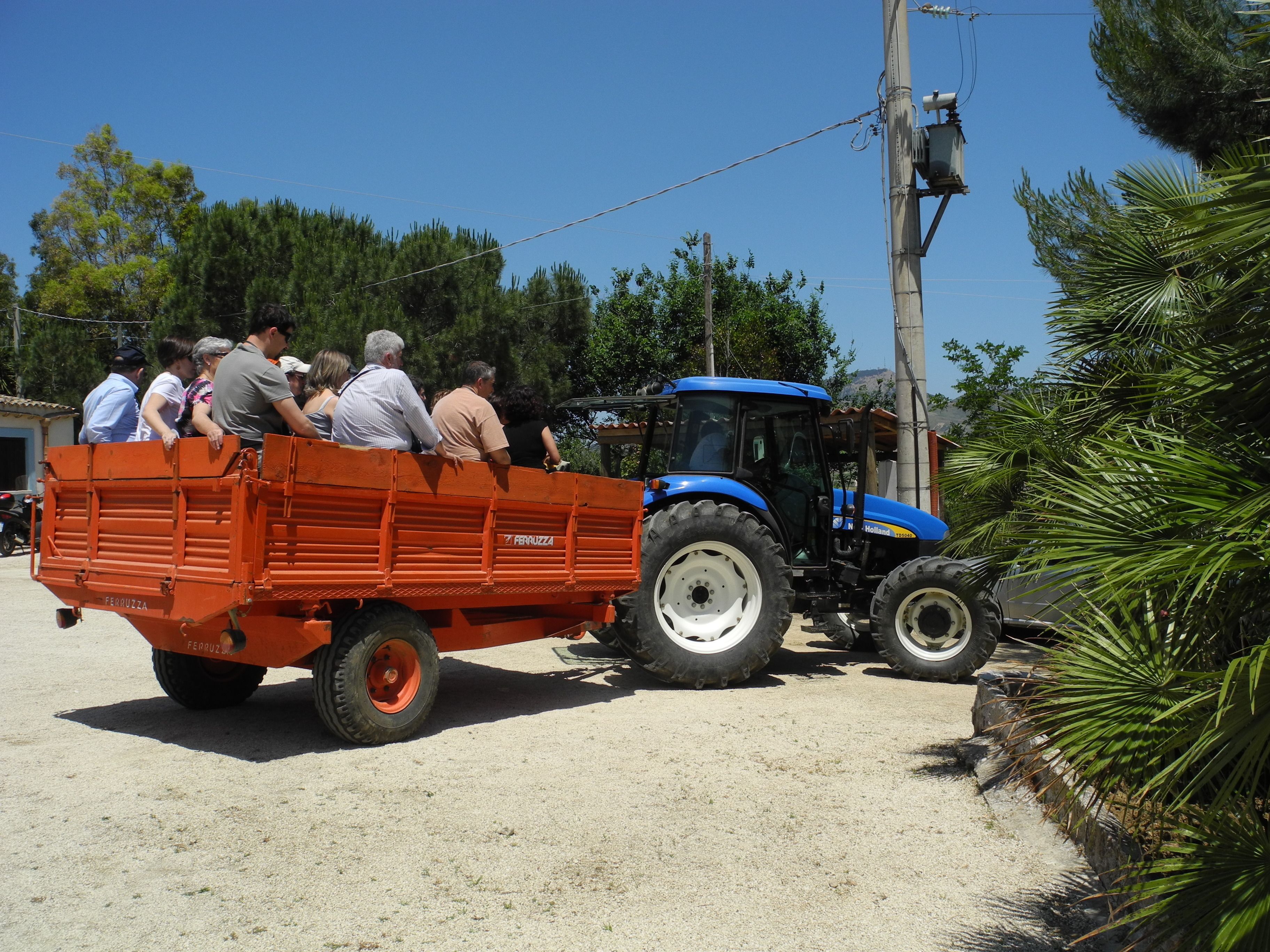 Een blauwe tractor met een rode aanhanger, vol met mensen.