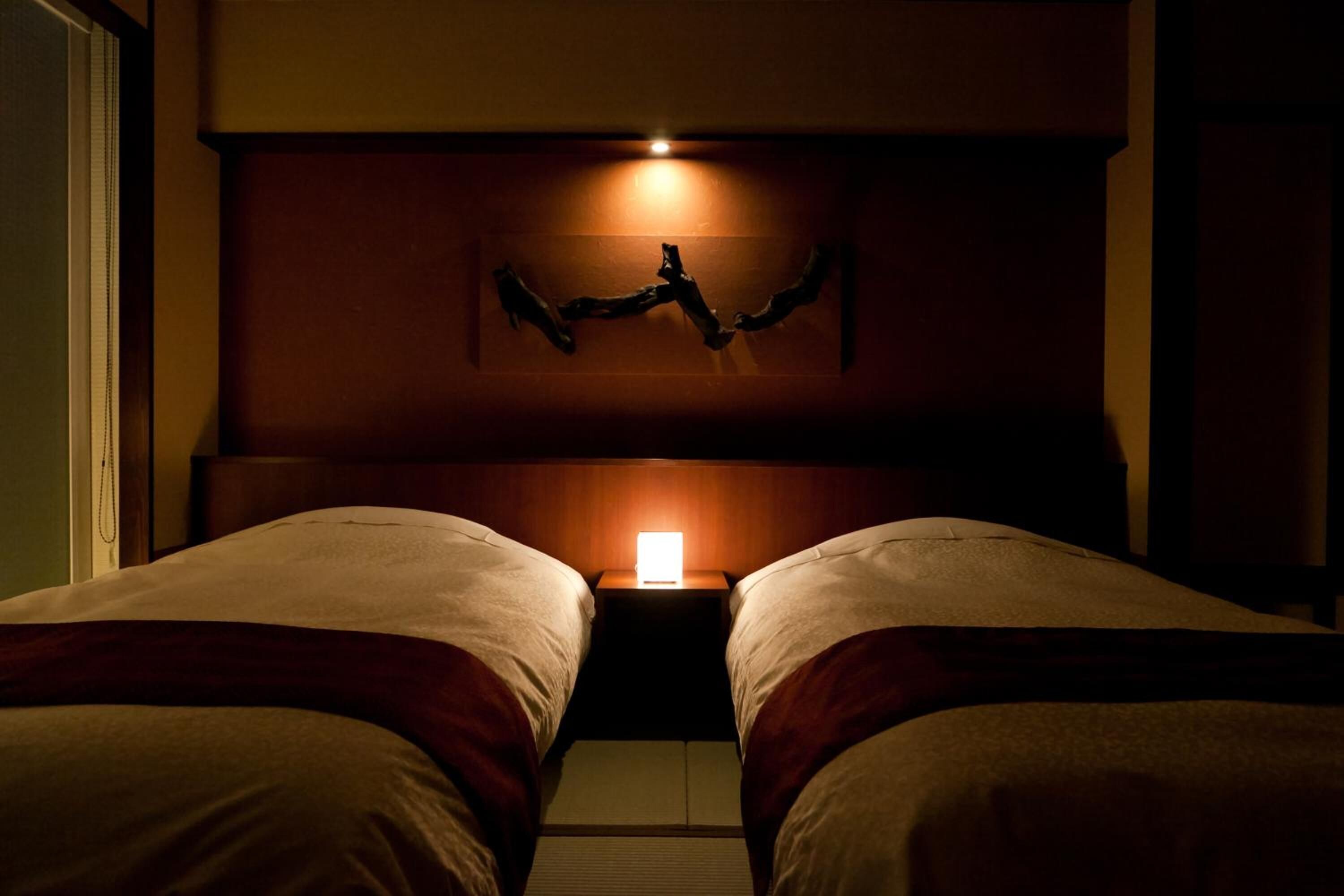 Habitación de hotel con dos camas, una mesita de noche con lámpara y un adorno en la pared.
