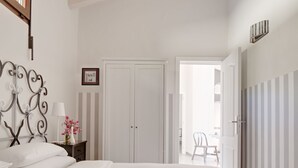 Een slaapkamer met twee bedden, een nachtkastje met een lamp en bloemen, een kledingkast en een deur naar een andere kamer.
