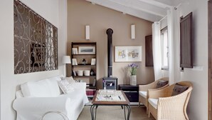 Een woonkamer met een witte bank, rieten stoelen, een salontafel, een boekenkast, een open haard en een decoratief wandobject.