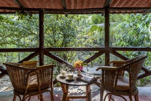 A wooden table with two wicker chairs, a vase with flowers, and two cups with steam rising from them. - Sunderban Tiger Camp (Gosaba)