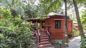 Un pequeño edificio de ladrillo rojo con una escalera que lleva a un porche, rodeado de exuberante follaje.