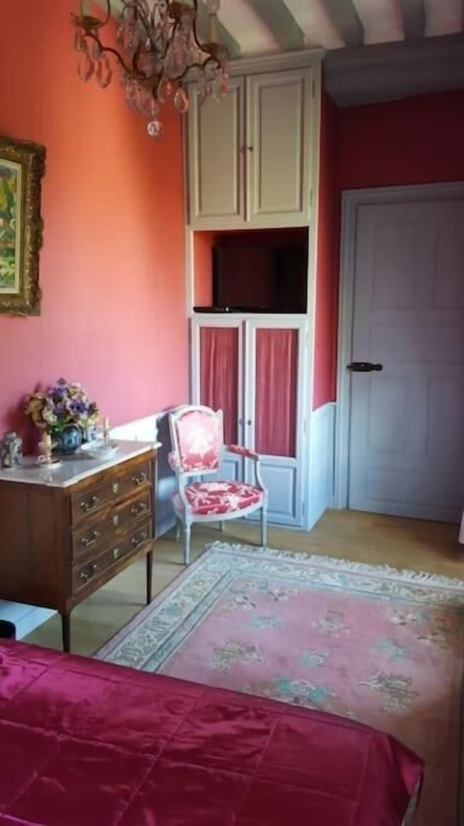 A bedroom with a bed, a dresser, a chair, a window with curtains, and a door.