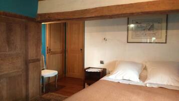 Una camera da letto con soffitto in legno, un letto con lenzuola bianche, un comodino, una sedia e una porta che dà su un'altra stanza.