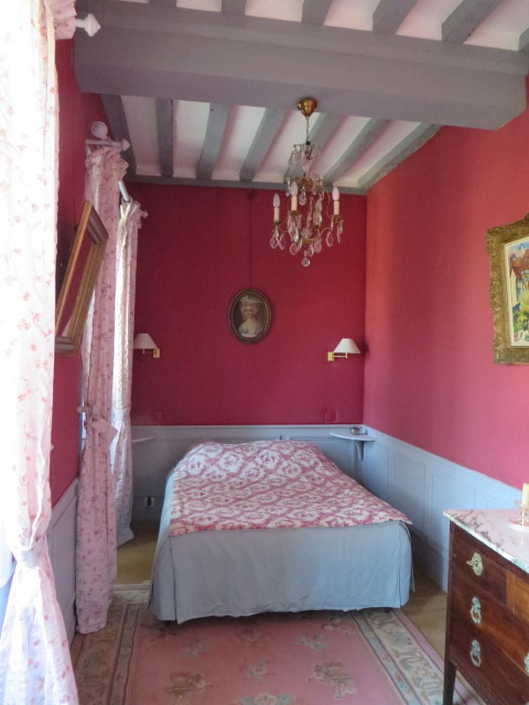 A bedroom with a bed, a dresser, a chandelier, and a red wall.