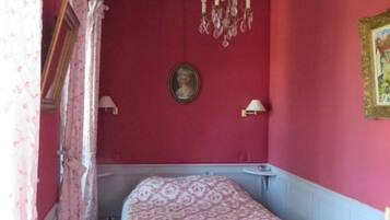 A bedroom with a bed, a dresser, a chandelier, and a red wall.