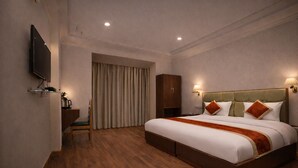 Habitación de hotel con una cama grande, un escritorio, una silla, un armario, un televisor y una cortina.
