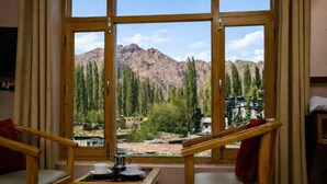 Habitación con un gran ventanal que ofrece vistas a la montaña. Hay dos sillas de madera con cojines y una pequeña mesa con una cafetera y tazas.