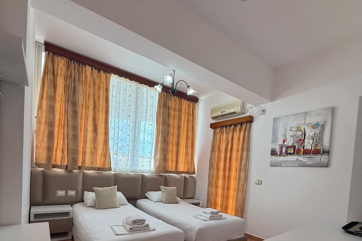 A modern hotel room with two beds, a desk, a chair, and a painting on the wall.