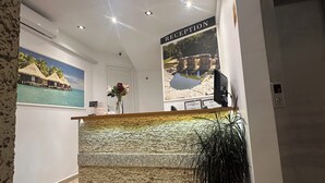 A reception area with a reception desk, a wall-mounted sign indicating 'RECEPTION,' a framed picture of a tropical scene, a potted plant, and a digital clock. - Hotel Oskar (Sarandë)