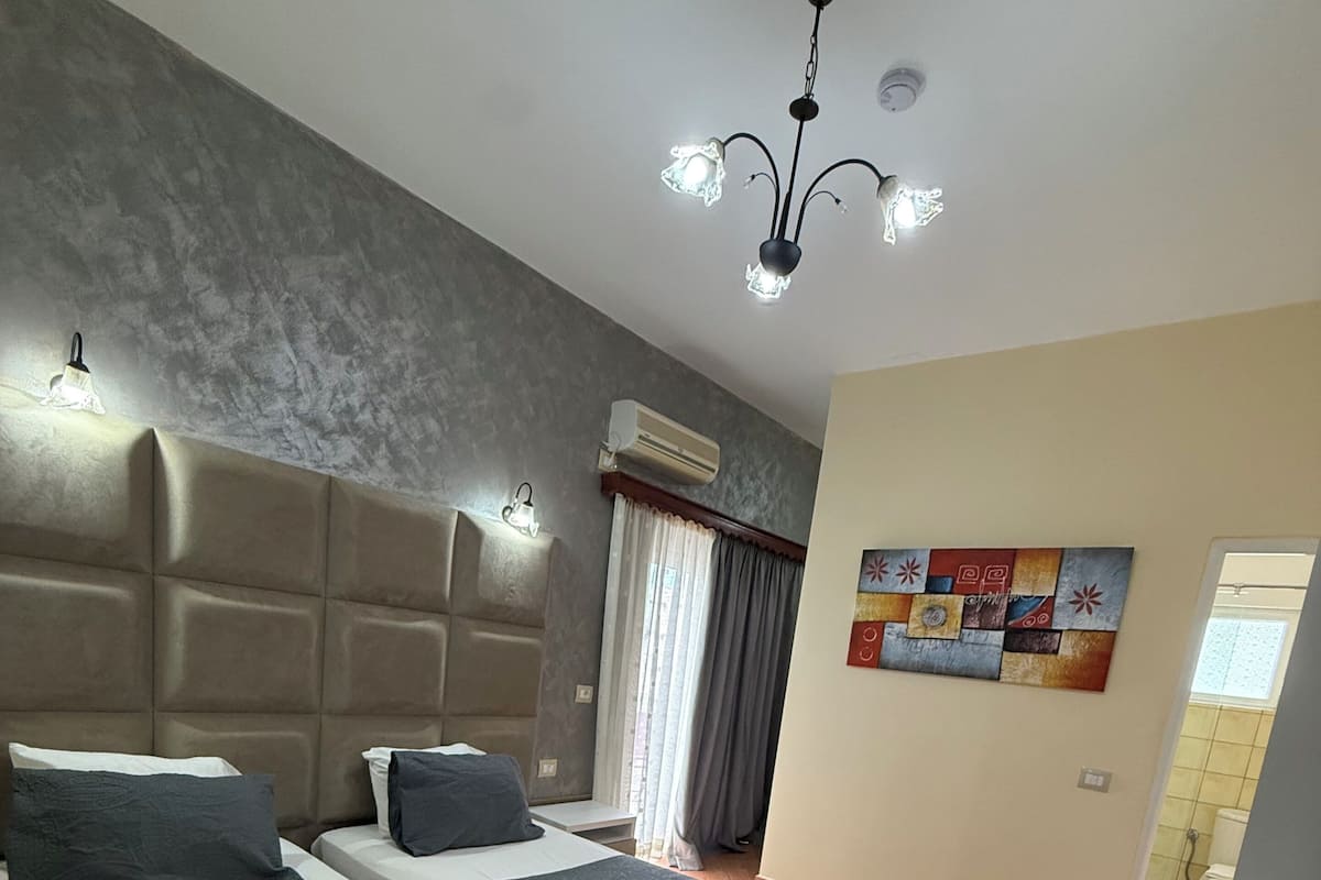A hotel room with two beds, a ceiling light, an air conditioning unit, and a wall art piece.