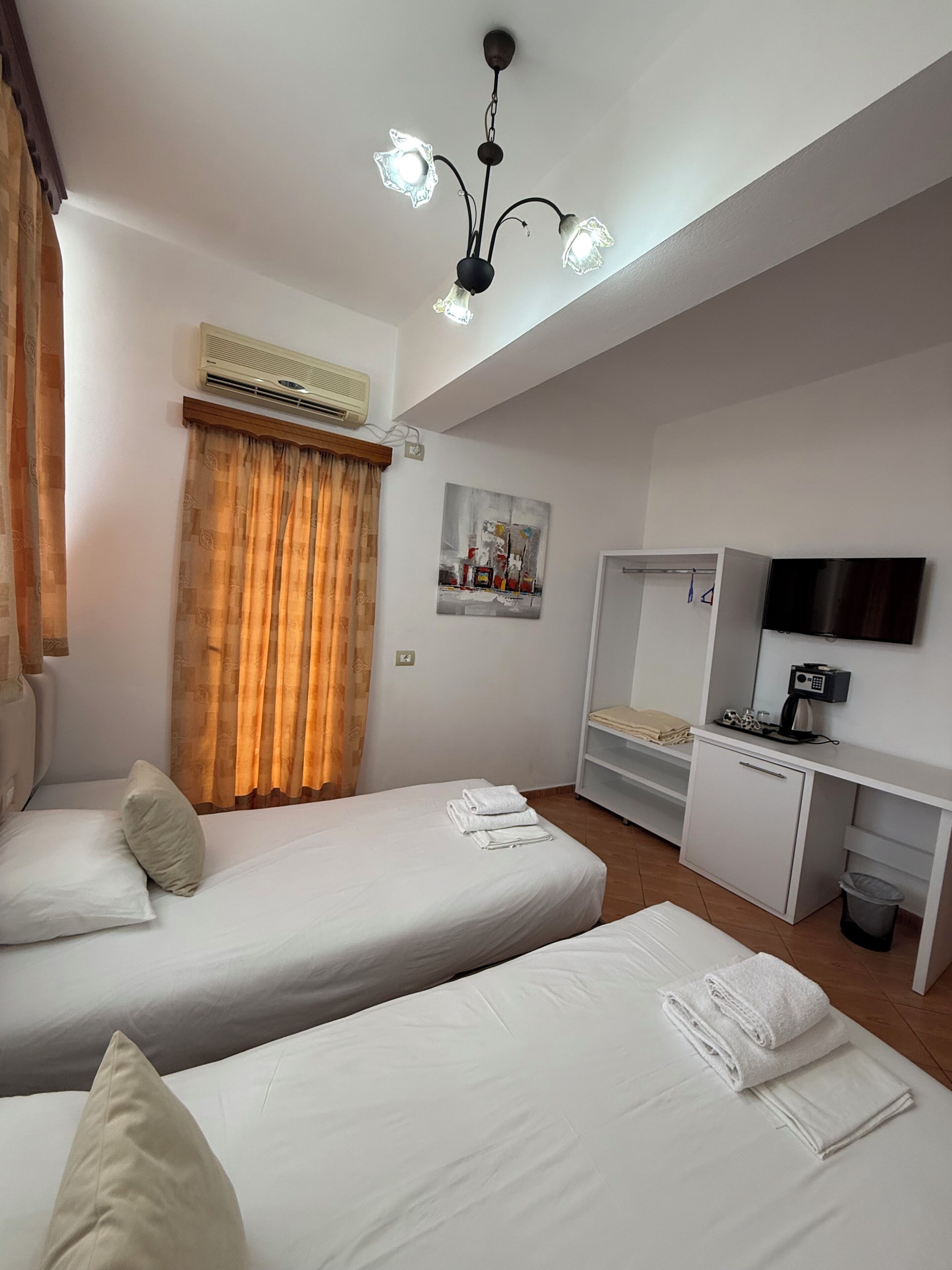 A hotel room with two beds, an air conditioning unit, a TV, a desk, and a painting on the wall.