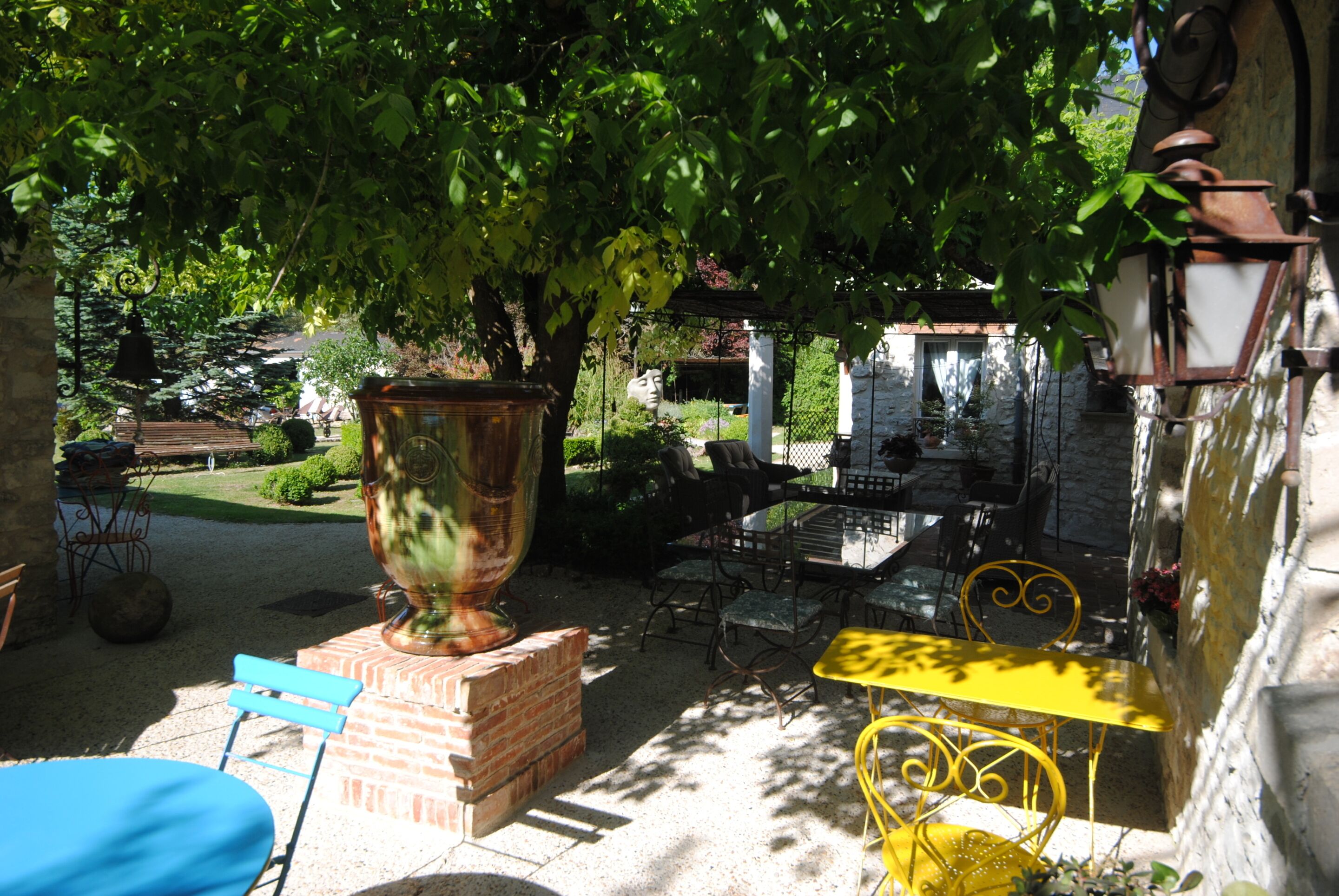 Un patio al aire libre con una mesa de ladrillo, sillas amarillas y una urna grande.