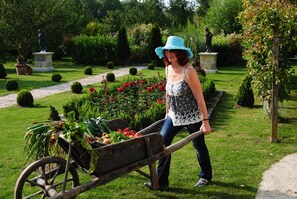 A garden with a statue, a woman pushing a wheelbarrow, and a pathway. - Les Insolites du Grand Logis (Marchais)