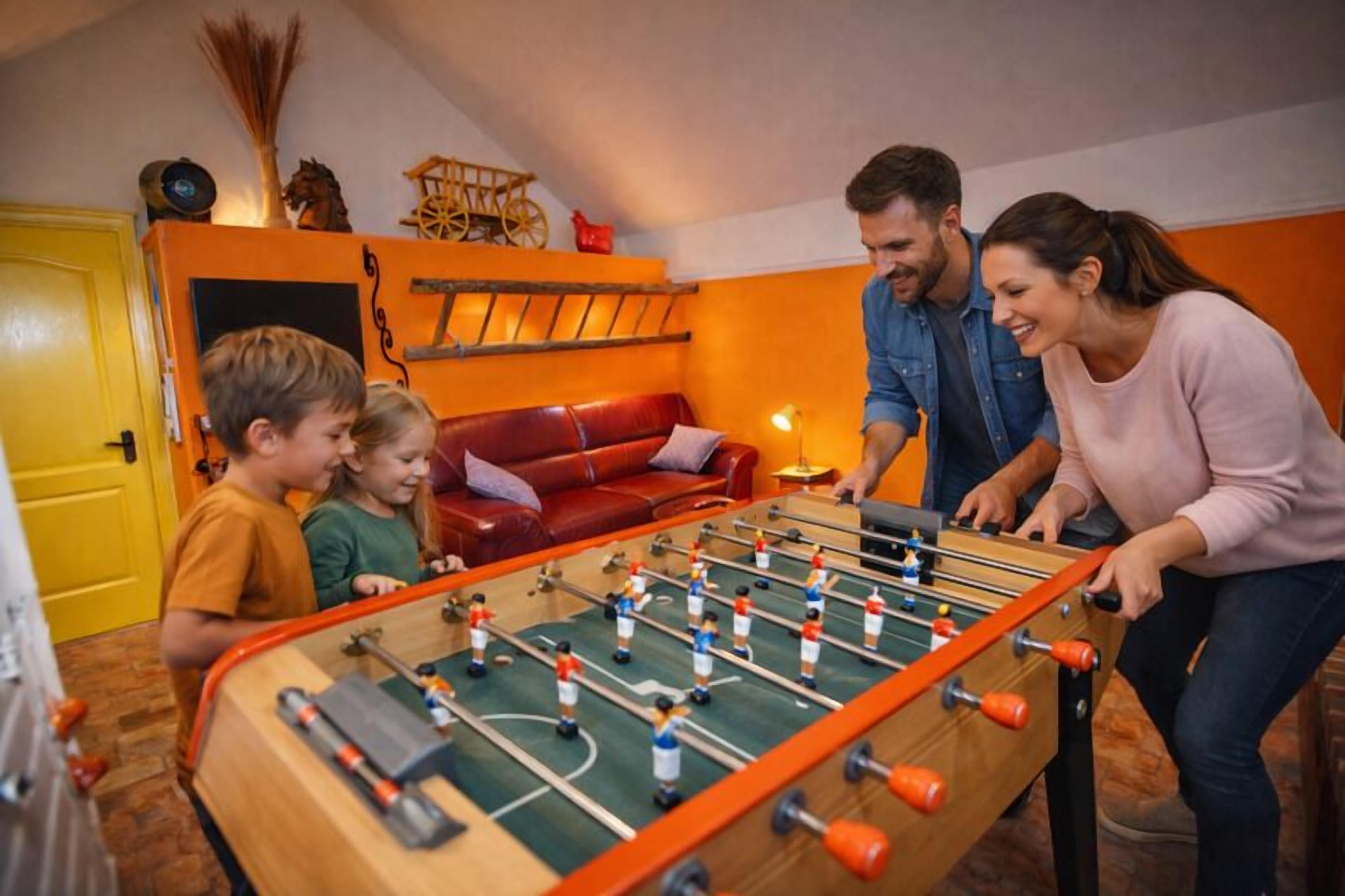 A room with a foosball table, a red leather couch, and a yellow door.