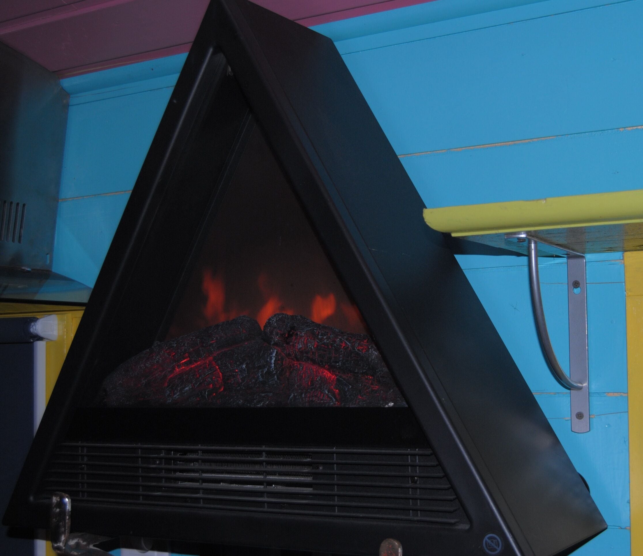 Une cheminée noire en forme de triangle, avec des flammes visibles à l’intérieur, placée devant un mur bleu.