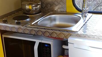 Una kitchenette compacta con microondas, estufa, fregadero y ventana con vista a árboles.