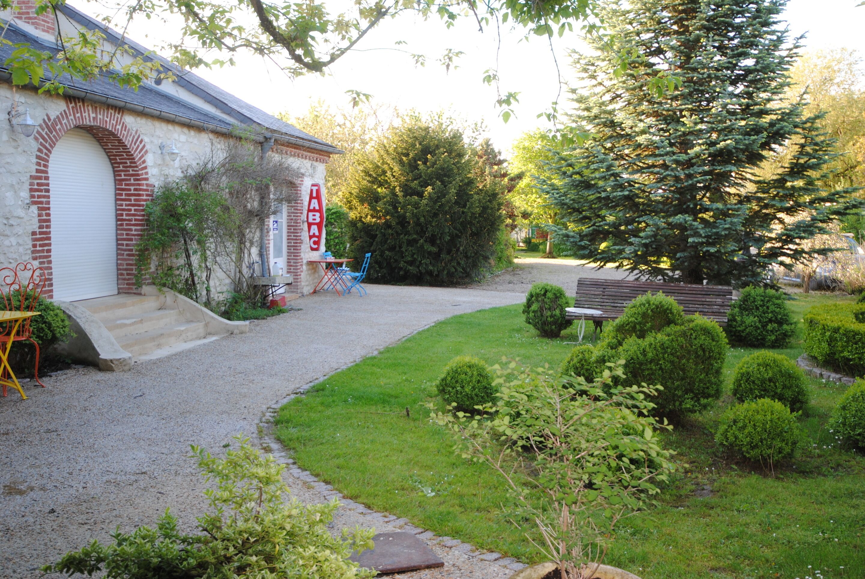 A house with a brick facade, a white garage door, and a gravel driveway leading to a front yard with a bench and a small table.