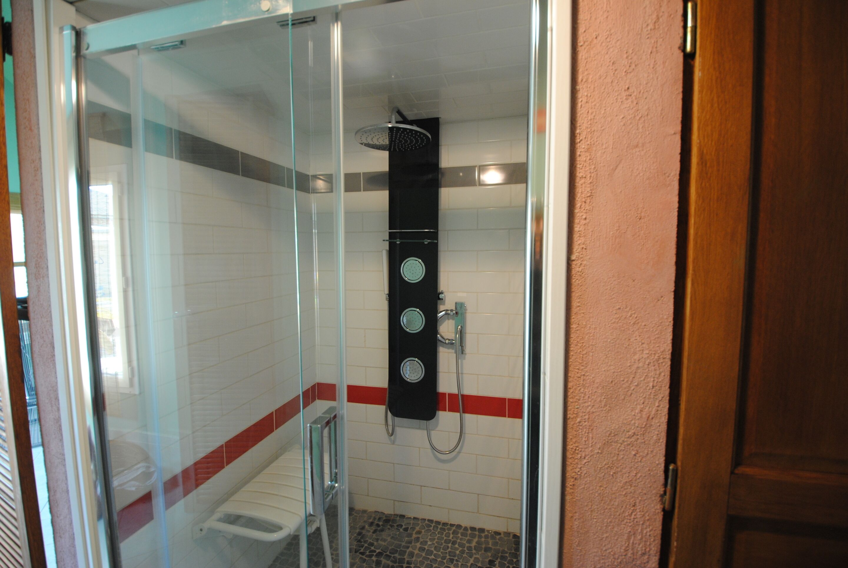 Een douchecabine met glazen wanden, een handdouche, een bedieningspaneel aan de muur en een betegelde vloer.