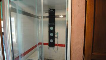 Een douchecabine met glazen wanden, een handdouche, een bedieningspaneel aan de muur en een betegelde vloer.