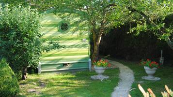 Una estructura de madera verde con un ventanal circular, rodeada de abundante vegetación y un sendero de grava.