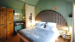 A bedroom with a bed, a wooden wardrobe, a bathroom with a sink and mirror, and a decorative wall panel. - Les Insolites du Grand Logis (Marchais)