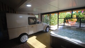 A hot tub and a vintage truck inside a room with large windows and a brick floor. - Les Insolites du Grand Logis (Marchais)