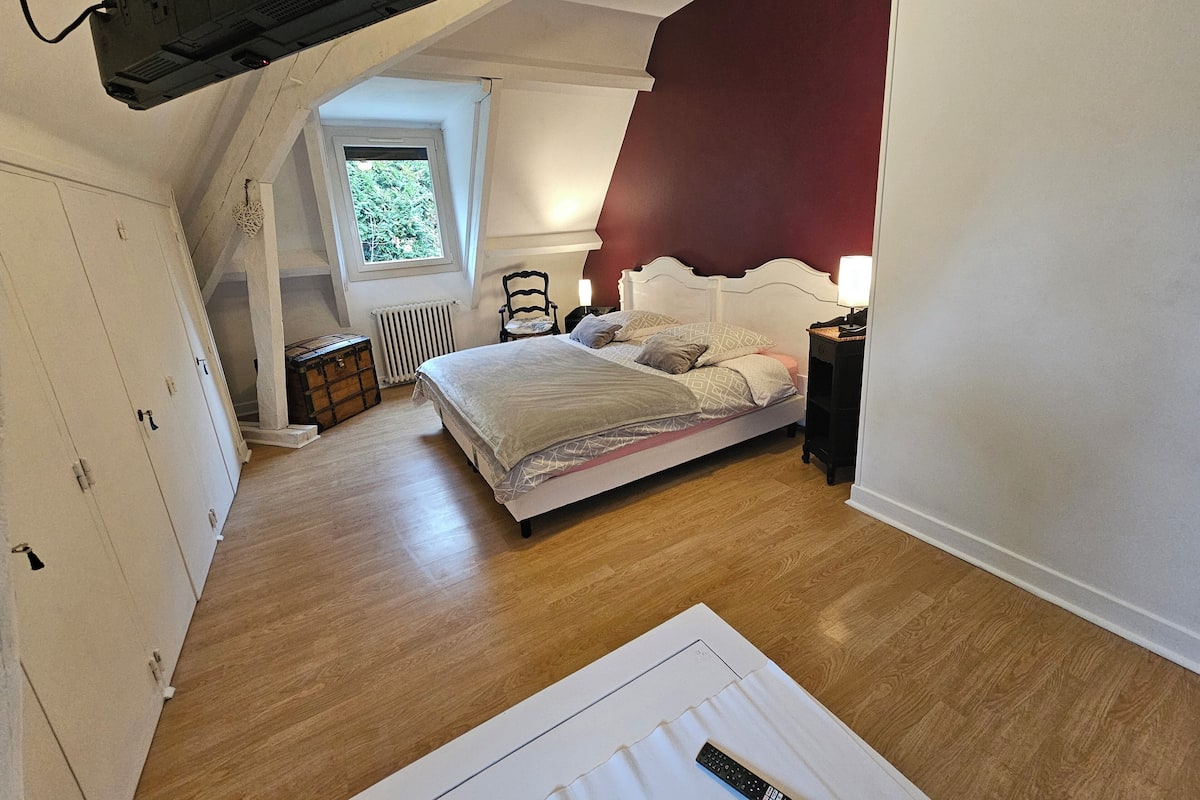 Ein Schlafzimmer mit Bett, einer Kommode, einem Heizkörper, einem Fenster und einem an der Wand befestigten Fernseher.