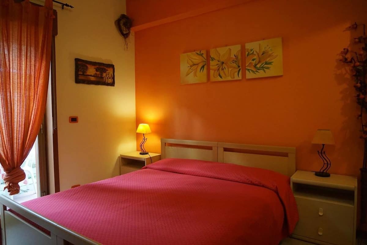 A bedroom with a bed, two bedside tables, a window with curtains, and wall art.