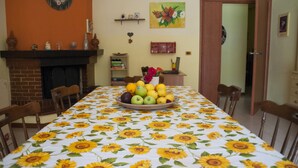 A dining room with a sunflower tablecloth, a fireplace, and a fruit bowl on the table. - B&B Sikily Naxos (Giardini Naxos)