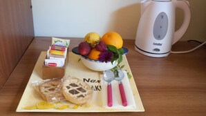 A breakfast setup with a bowl of fruit, a pastry, a box of Delicande chocolates, a kettle, and a napkin with utensils on a wooden table. - B&B Sikily Naxos (Giardini Naxos)