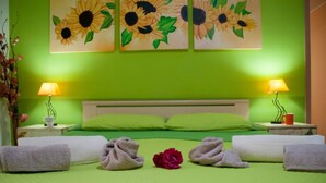 A neatly made bed with green bedding, two bedside lamps, a floral arrangement, and a painting of sunflowers on the wall. - B&B Sikily Naxos (Giardini Naxos)