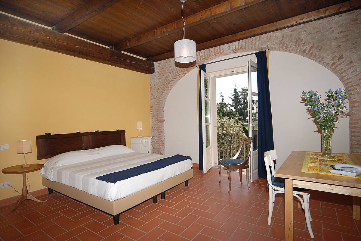 A bedroom with a bed, bedside table, lamp, and a view of the outdoors through an open door.