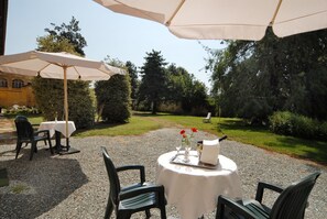 An outdoor patio with a round table set for two, surrounded by chairs, under a large umbrella. - Agriturismo Camisassi (Saluzzo)