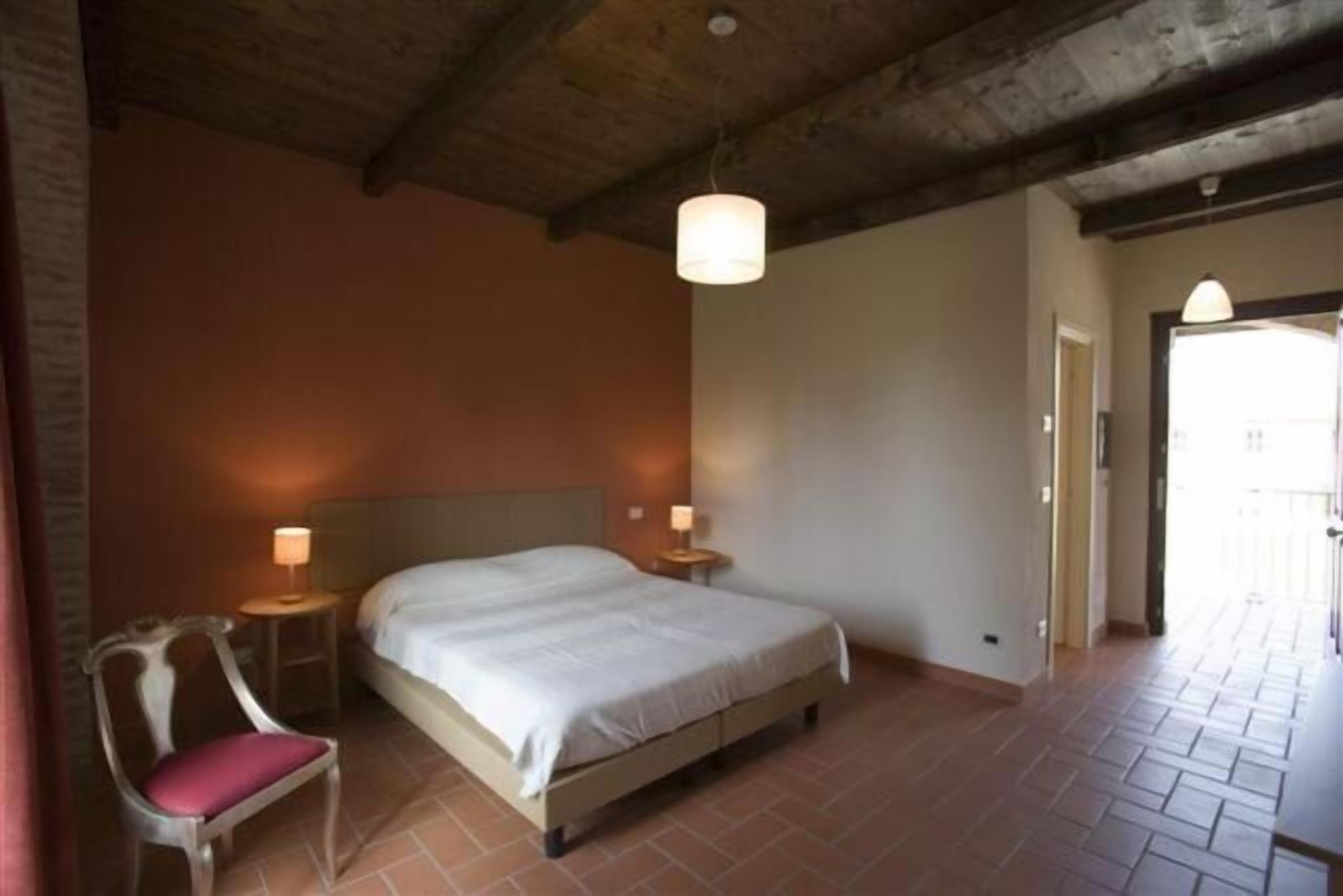 Ein Schlafzimmer mit einem Bett, einem Sessel, zwei Nachttischen und einer Decke mit sichtbaren Balken.