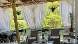 A covered outdoor seating area with wicker furniture, a table with a vase, and a motorcycle parked outside. - Hôtel bar b’rock (Saint-Martin-sous-Vigouroux)