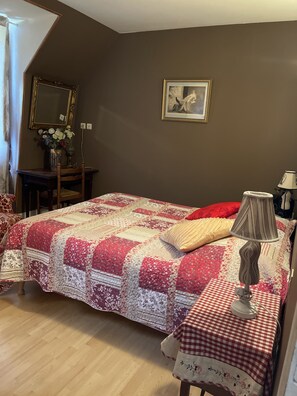 Een slaapkamer met een bed, een bureau, een stoel, een lamp en een schilderij aan de muur.