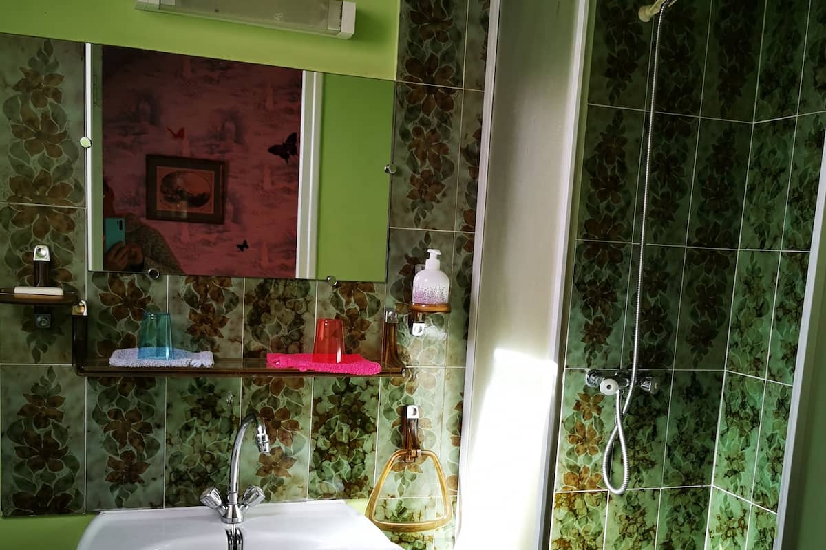 Ein Badezimmer mit Waschbecken, Spiegel, Dusche und grün gefliesten Wänden.