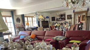 A living room with a red leather sofa, wooden coffee tables with teapots, and a chandelier. - Hôtel bar b’rock (Saint-Martin-sous-Vigouroux)