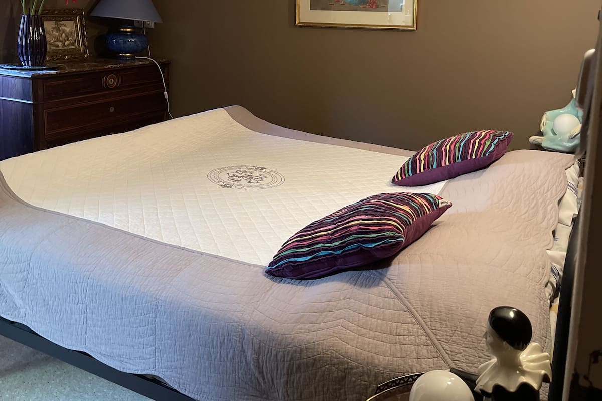 Ein Schlafzimmer mit einem Bett, Kissen, einem Schminktisch, einer Lampe, einem gerahmten Bild und einer Blumenvase.
