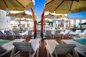 A poolside area with white lounge chairs and beige umbrellas. - Vela Garden Resort (Cesme)