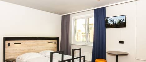 A modern hotel room with a wooden headboard bed, a small stool, two orange ottomans, and a round table.