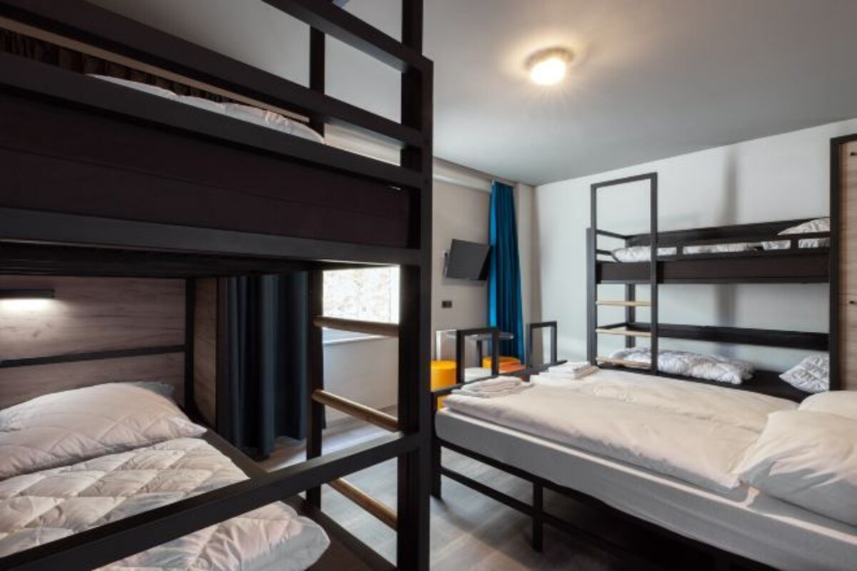 Une chambre avec un lit superposé, une télévision, une fenêtre avec des rideaux et un luminaire au plafond.