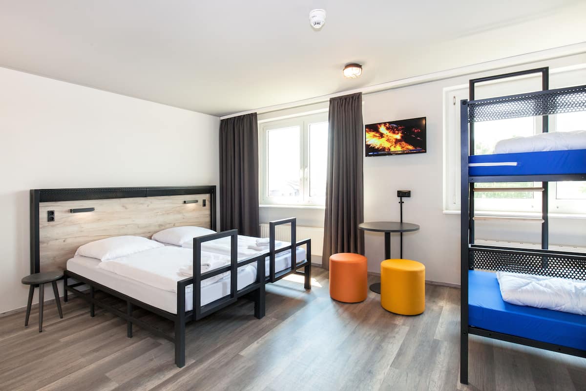 Une chambre d’hôtel moderne avec un lit doté d’une tête de lit en bois, un lit superposé, une petite table ronde et un téléviseur fixé au mur.