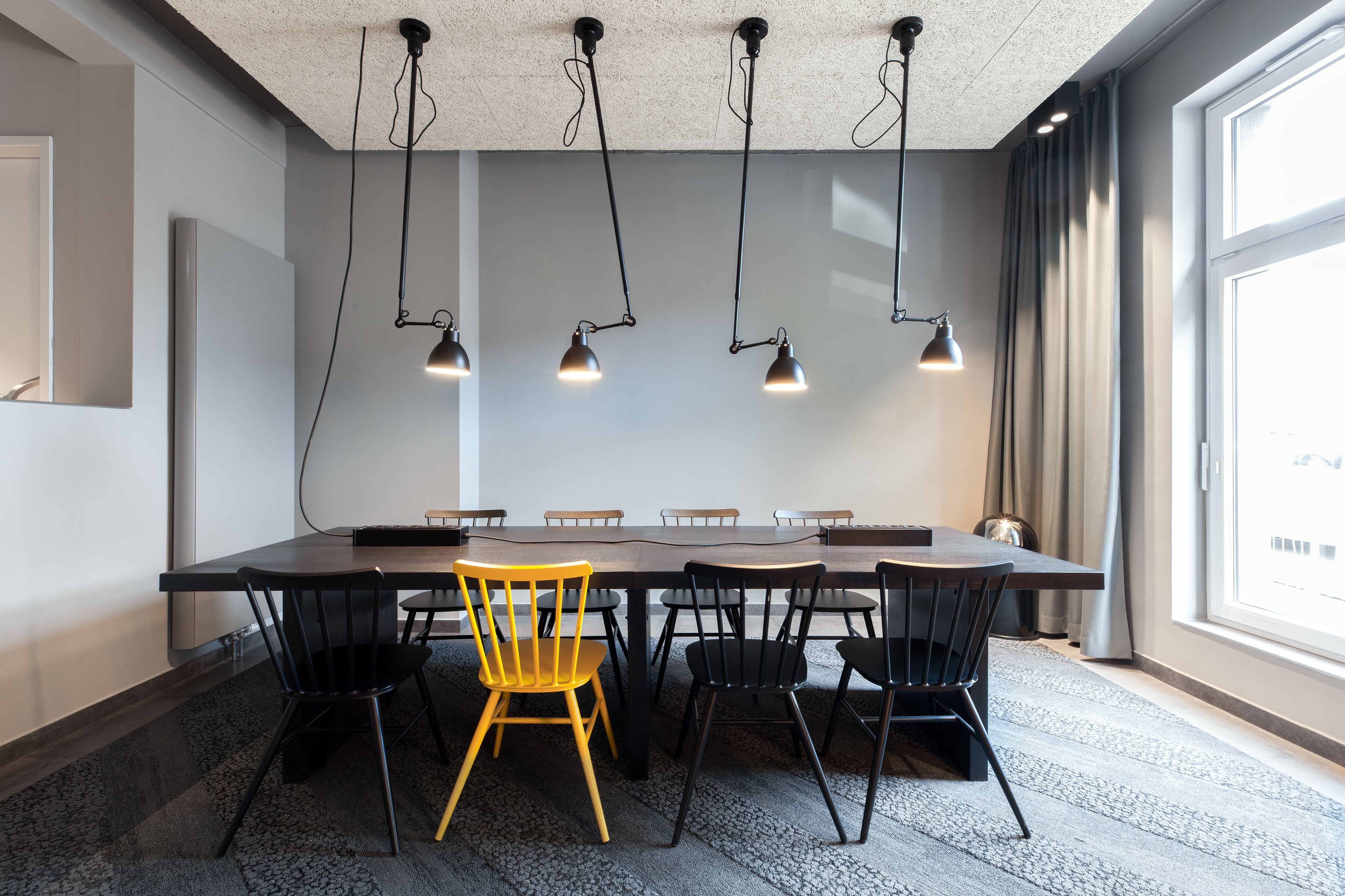 Une salle de conférence avec une longue table, des chaises noires et jaunes, et des luminaires suspendus.