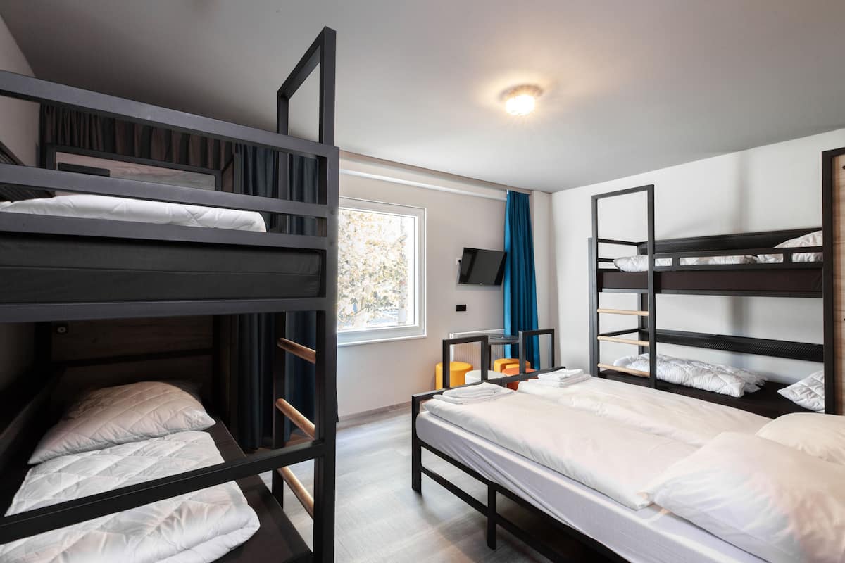 Une chambre de dortoir avec des lits superposés, une fenêtre avec des rideaux, un téléviseur à écran plat et une petite table avec une chaise.